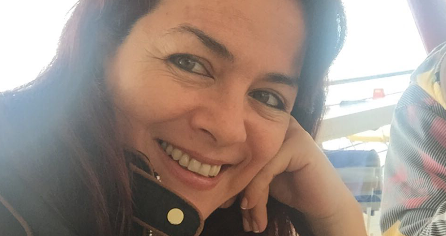 A woman smiling, resting her head on her hand, with a bright background.